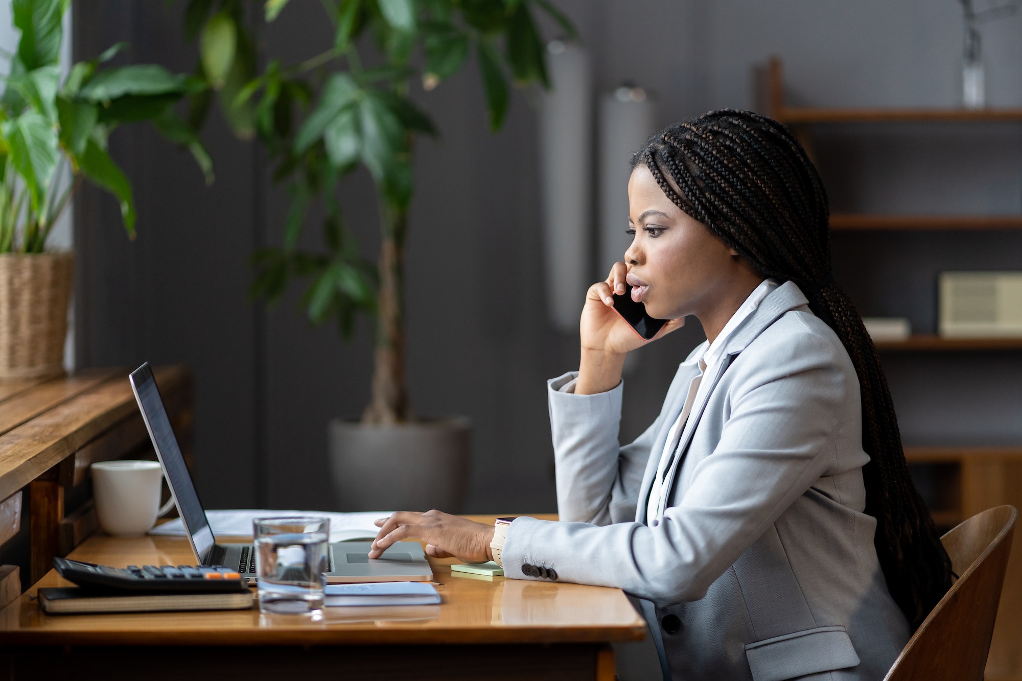 Afro female business consultant interacting with client over phone and entering data on laptop